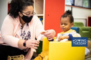 A teacher guides the hand of a preschool boy who is visually impaired over a toy so that he can experience it.