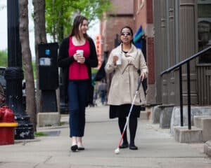 A blind woman walking with a friend and drinking coffee