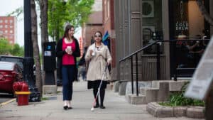 A blind woman walking with a friend and drinking coffee