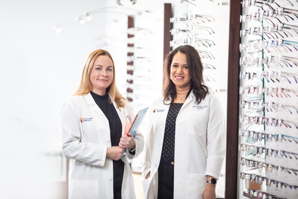 Two doctors stand in a low vision clinic against the backdrop of a wall of glasses