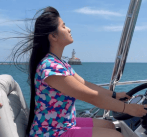 A teenage girl who is blind steers a yacht on Lake Michigan. In the distance is a lighthouse.