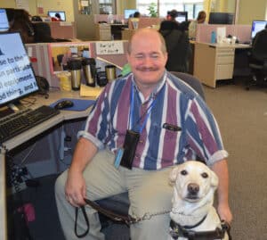 disabled man using assistive tech with his guide dog next to him