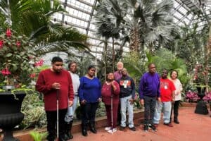 A group of participants from the Adult Living Skills program stand together in front of palm trees in a greenhouse at Garfield Park Conservatory.