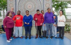 A group of participants from the Adult Living Skills program stand together in front of a mosaic wall with circular patterns at Garfield Park Conservatory.