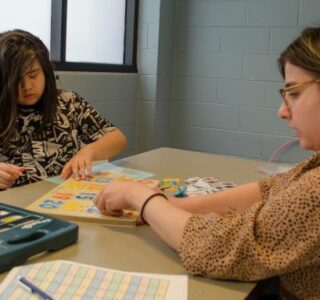 Dani Krause sits at a table with a student working on the alphabet.