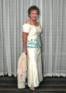 Leticia Freihaut standing in fron tof a curtain in a floor length white dress.