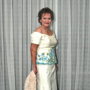Leticia Freihaut standing in fron tof a curtain in a floor length white dress.