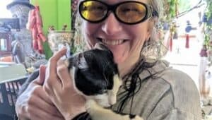 Liz wears large glasses with yellow lenses and holds a black and white cat.