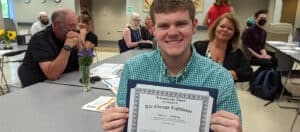 A college student with a visual impairment holds up his scholarship certificate