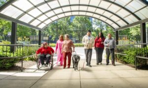 Six people walk and talk under the archway of The Chicago Lighthouse. One woman uses a wheelchair, one uses a guide dog and two men who are blind use white canes.