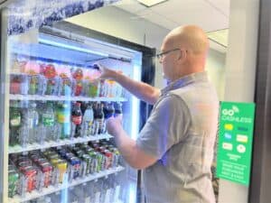 A bald man wearing glasses restocks a vending machine.