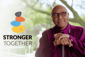 Image of a smiling man in a purple shirt, sitting with hands clasped over a white cane, next to the logo "Stronger Together" with three colorful, smiling faces stacked above the text.