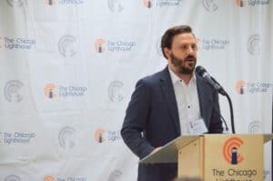 Peter speaking at a podium with The Chicago Lighthouse logos in the background. He has short brown hair and a well-kept beard.
