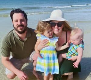 Peter, his wife, and two children smile for a photo on a sunny beach.
