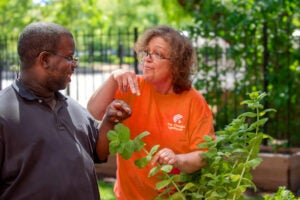 A woman in an orange Chicago Lighthouse shirt points expressively at a plant while talking to a man.