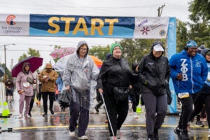 A woman who is blind walks with a guide and other participants in the Rise to Shine Race wearing rain ponchos and carrying umbrellas