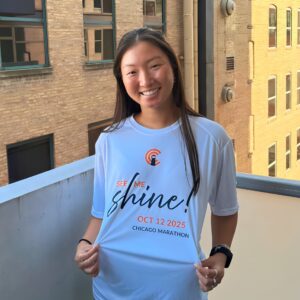 A young woman smiles while wearing a t-shirt with 'Shine' on it.