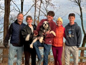 A family poses in front of a lake with a cute dog.