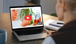 A woman watches a laptop screen with a youtube video showing assistive technology.