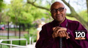 A man who is visually impaired rests his hands on top of his white cane.